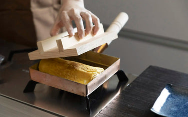 Placing wooden lit on top of cooking tamagoyaki